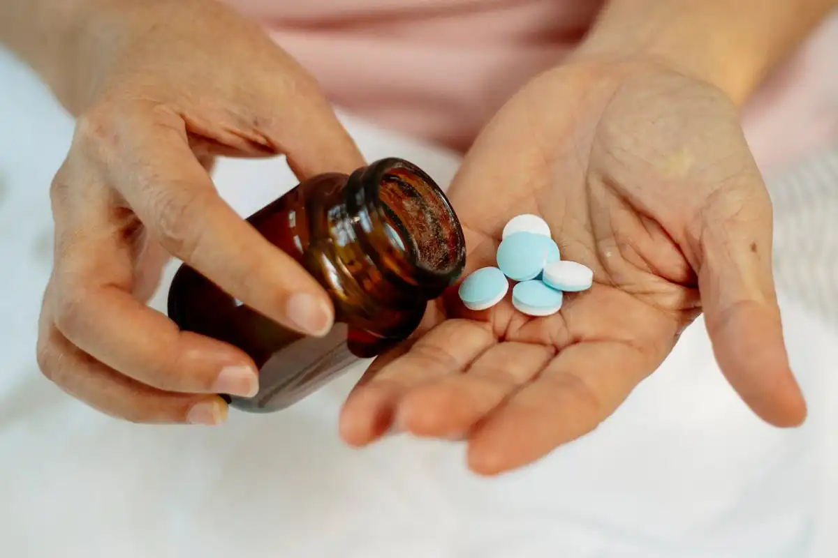 Close-up of hands holding pills from a dark glass bottle, symbolizing prescription drugs