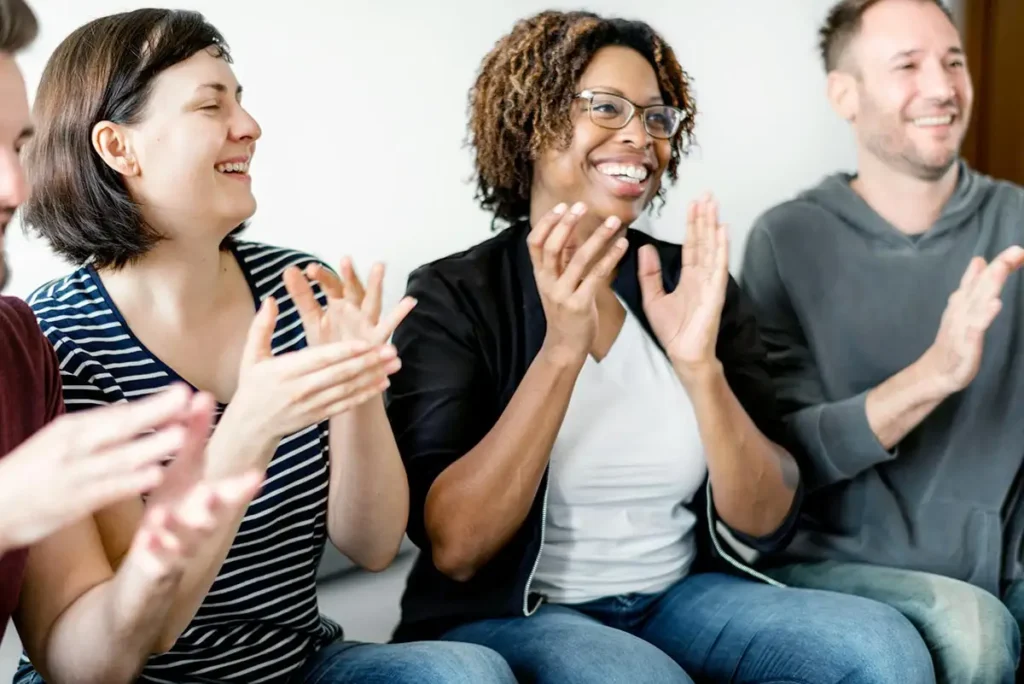 A diverse group of individuals enthusiastically clapping together, symbolizing support and community in a recovery setting.