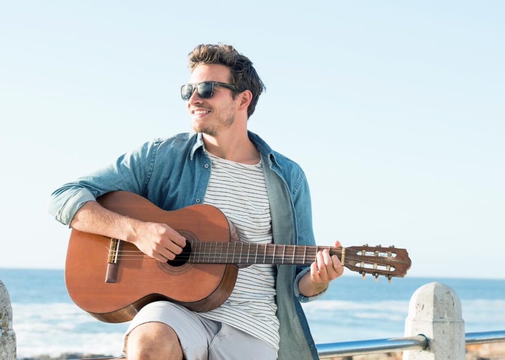 man playing a guitar near the ocean