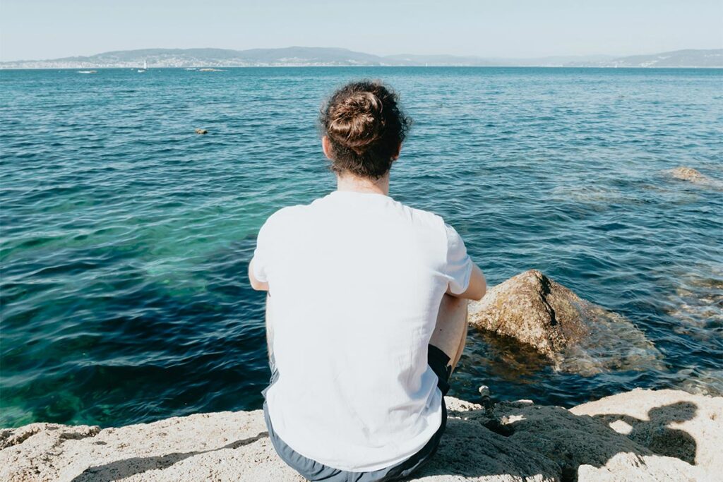 a man sitting on a rock looking out at the ocean