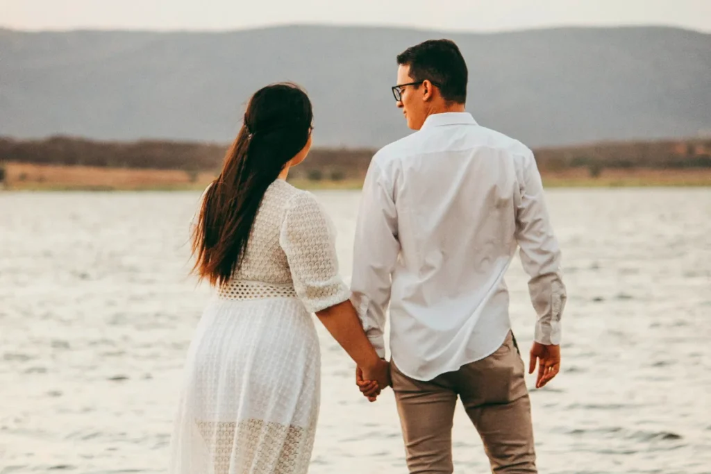 a couple near the ocean holding hands wearing white clothes