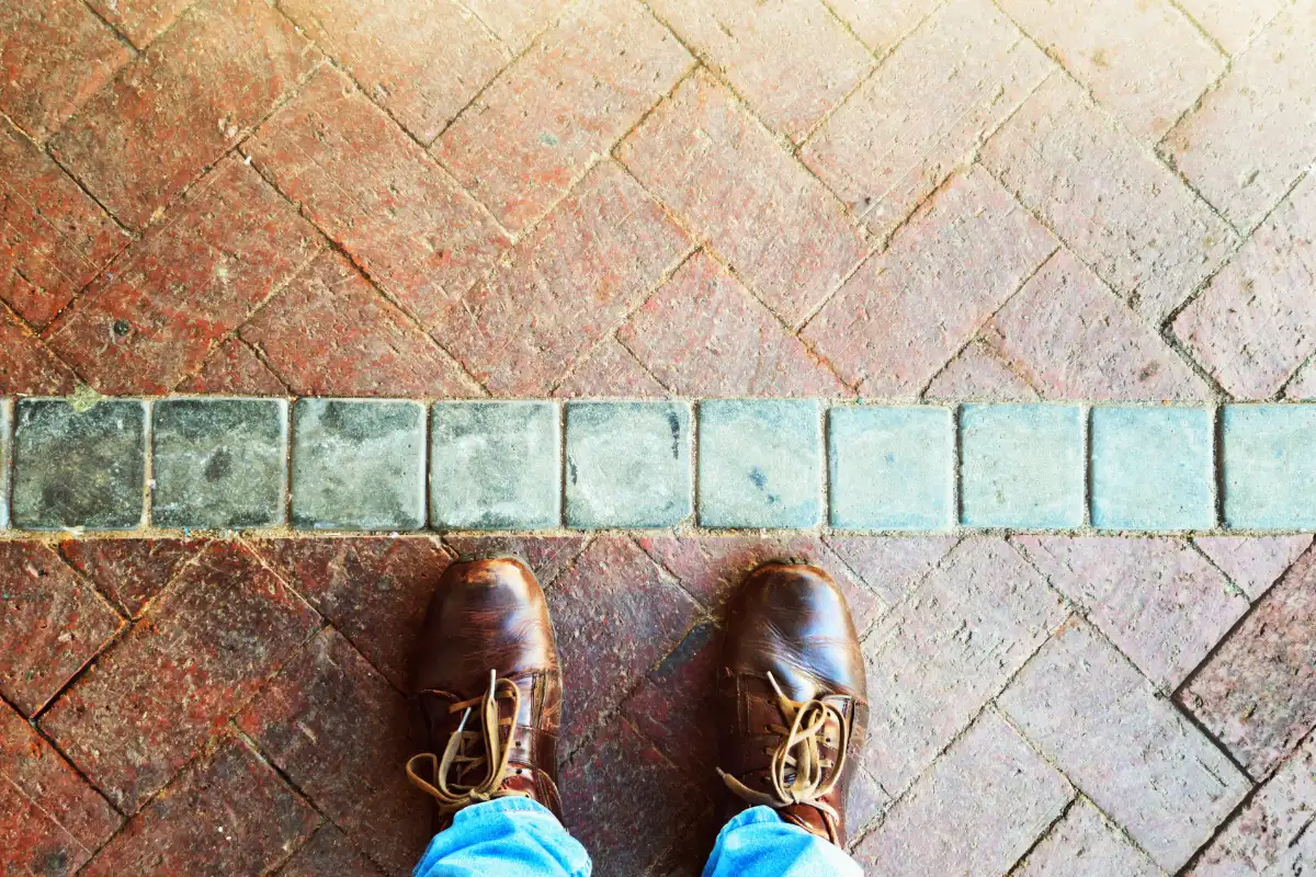 Man's feet behind boundary line in brick paving