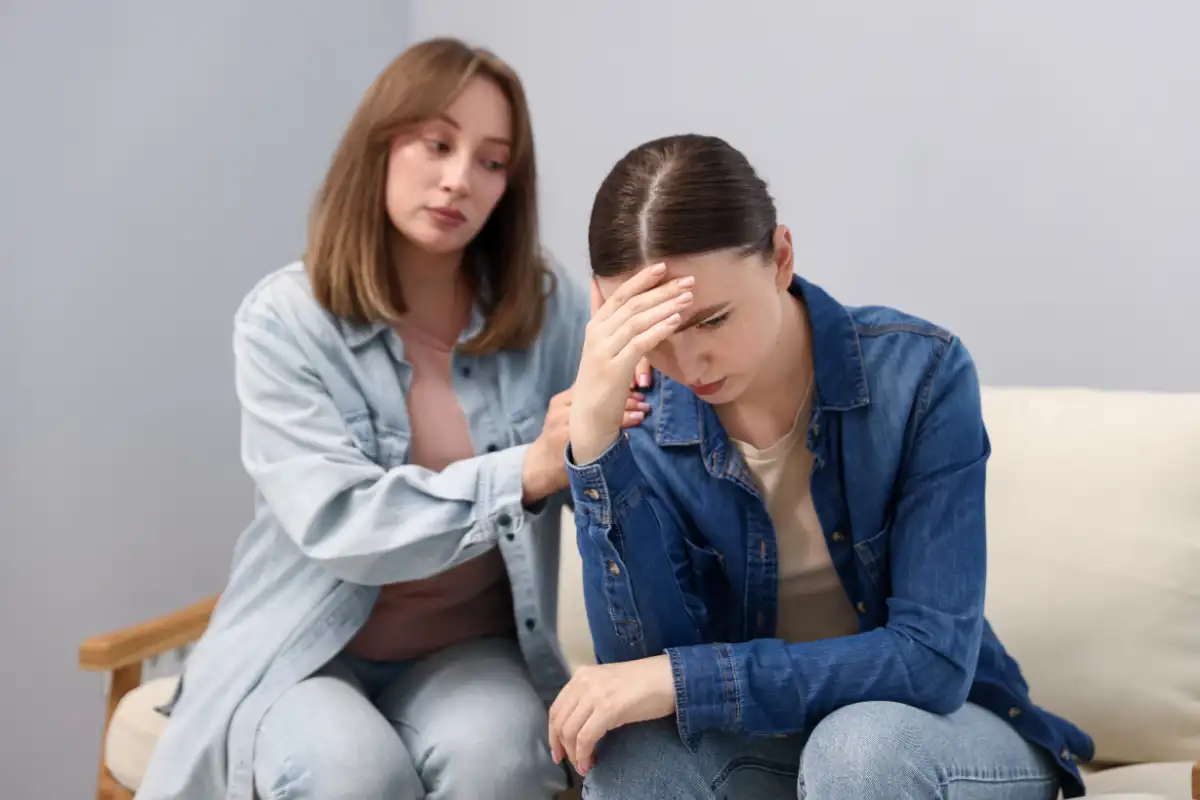 Woman Apologizing to Her Offended Friend on Armchair near Grey Wall at Home