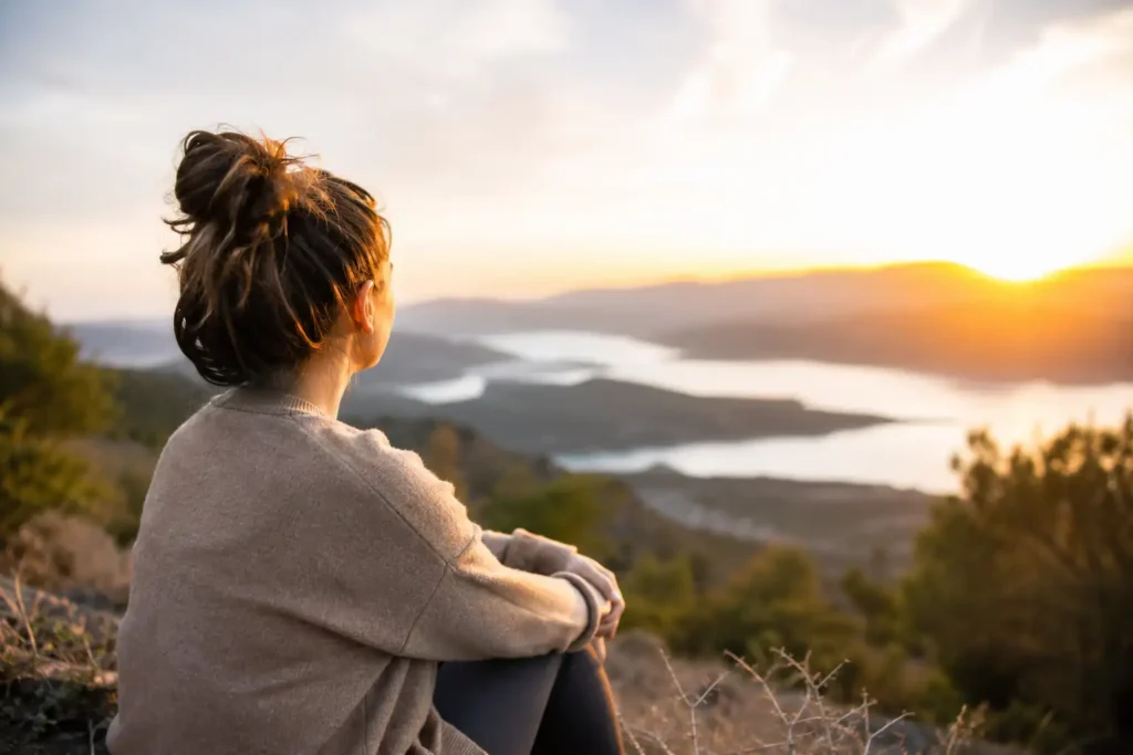 Young woman overlooking the ocean at sunrise, reflecting peacefully while embracing healing and recovery.